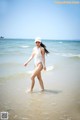 A woman in a white bathing suit walking in the ocean.