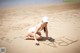 A woman in a white bathing suit and hat writing in the sand.