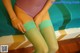 A woman in a purple bodysuit and green stockings sitting on a bed.