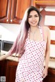 A woman in a pink and white polka dot dress posing in a kitchen.