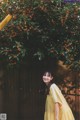 A woman in a yellow dress standing in front of a tree.