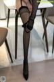 A woman in black stockings and high heels sitting at a table.