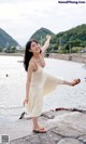 A woman in a white dress standing on a pier by the water.