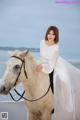 A woman in a white dress riding a white horse on the beach.