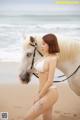 A woman in a white bikini standing next to a white horse.