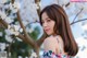 A woman in a floral dress standing in front of a tree.