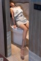 A woman in a white dress sitting on a toilet.