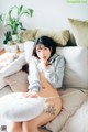 A woman sitting on top of a white couch next to pillows.