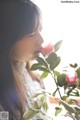 A woman smelling a pink flower in front of a window.