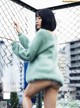 A woman in a green sweater leaning against a fence.