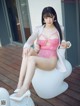 A woman in a pink lingerie sitting on a white chair.