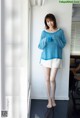 A woman standing in front of a white wall wearing a blue sweater.