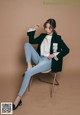 A woman sitting on a chair wearing a black blazer and jeans.