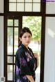 A woman wearing a black and purple kimono standing in front of a window.