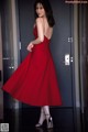 A woman in a red dress standing in front of a door.