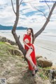 A woman in a red dress sitting on a tree by the beach.