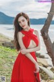 A woman in a red dress posing by the water.