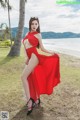 A woman in a red dress posing on the beach.