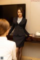 A woman in a business suit standing in front of a television.