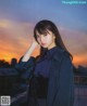 A woman standing on top of a roof next to a sunset.