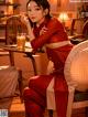 A woman in a red dress sitting at a table with a drink.