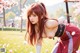 A woman in a red outfit poses with a sword in a grassy field with cherry blossoms.