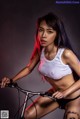 A woman in a white tank top riding a bike.