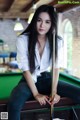 A woman sitting on top of a pool table holding a cue.