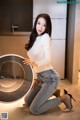 A woman kneeling on the floor next to a washing machine.