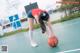 A woman in a red shirt and blue shorts holding a basketball.